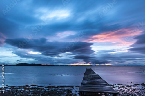 View of a pier on a lake at dusk, beneath a dramatic, moody sky