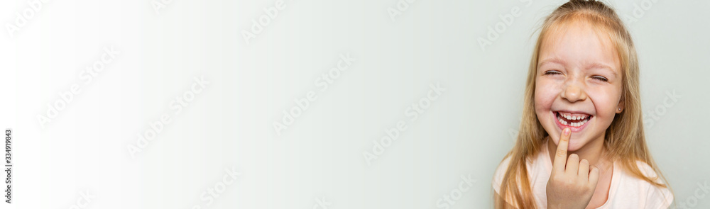 Kid showing the first milk tooth. Change teeth concept. Cute little girl with blonde hair on gray background with copy space. Horizontal long banner for web design Kid showing the first milk tooth. Change teeth concept. Cute little girl with blonde hair on gray background with copy space. Horizontal long banner for web design