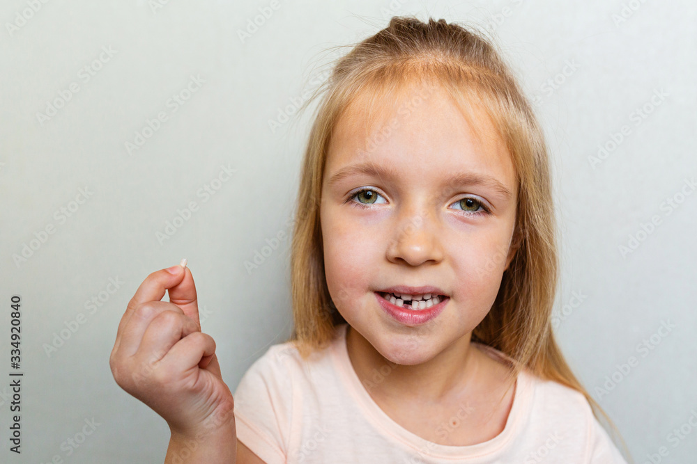 Kid showing the first milk tooth. Change teeth concept. Cute little girl with blonde hair on gray background with copy space. Kid showing the first milk tooth. Change teeth concept. Cute little girl with blonde hair on gray background with copy space.