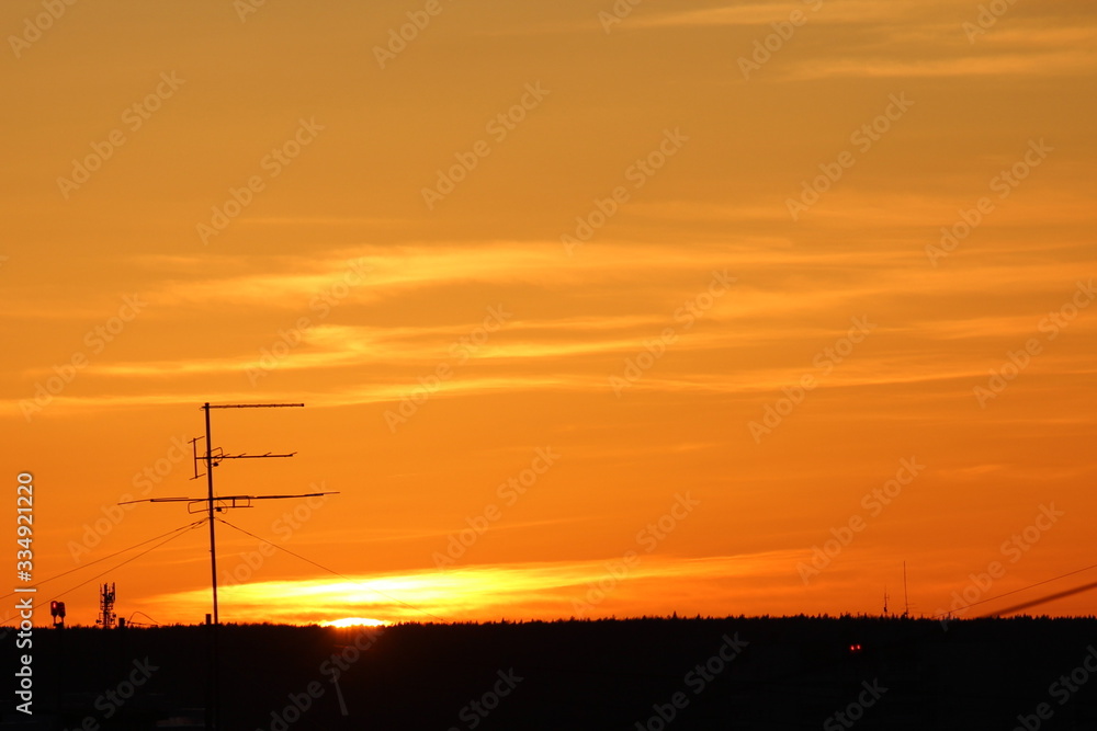 Sun below the horizon and television antenna in the background clouds in the fiery dramatic orange sky at sunset or dawn backlit by the sun. Place for text and design.