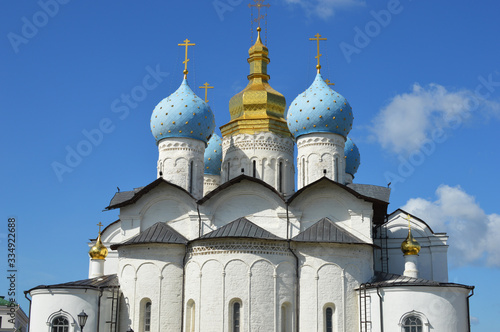 Front view of a christian church with white walls, blue and gold domes against a blue sky