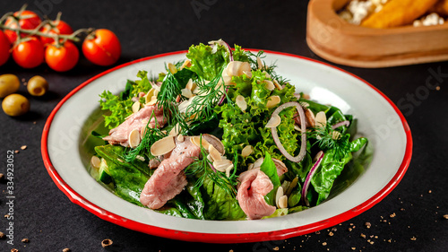Norwegian cuisine. Salad mix of lettuce, red onion, pickled veal and balsamic sauce. Serving dishes in a restaurant in a white plate. black background. copy space text