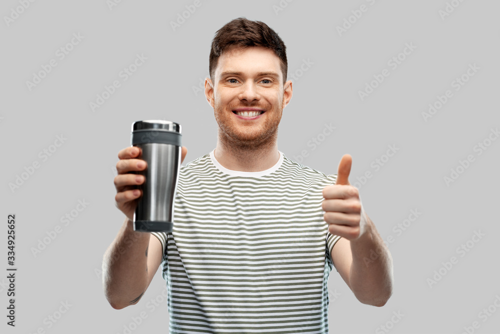 eco living and sustainability concept - happy smiling young man with thermo cup or tumbler for hot drinks showing thumbs up over grey background eco living and sustainability concept - happy smiling young man with thermo cup or tumbler for hot drinks showing thumbs up over grey background