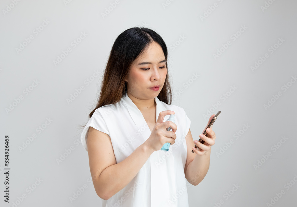 Close up of Asian girl wearing protective mask using alcohol gel to clean Mobile phone with copy space, isolated on white. Concept of woman washing Mobile phone with to avoid Corona virus Close up of Asian girl wearing protective mask using alcohol gel to clean Mobile phone with copy space, isolated on white. Concept of woman washing Mobile phone with to avoid Corona virus