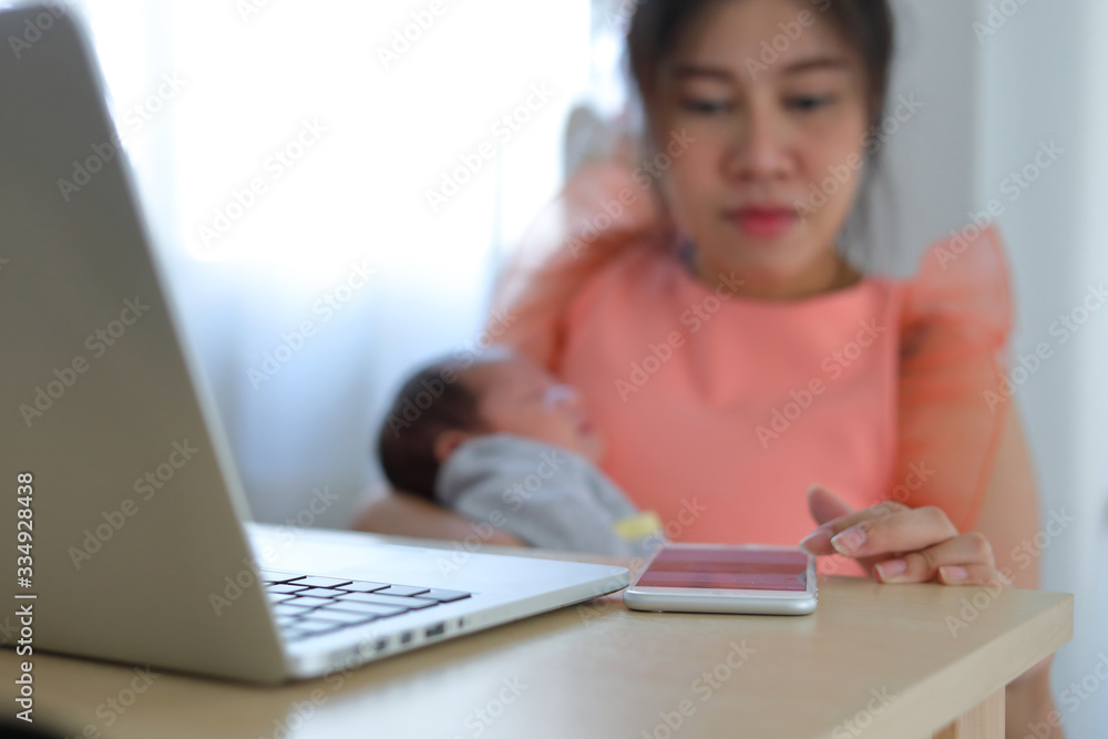 Fototapeta premium mother playing mobile phone in business home office with cute baby newborn sleeping