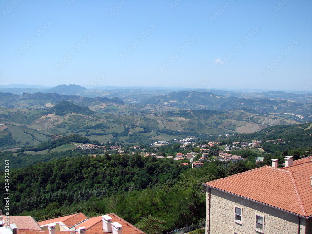 Panorama of blue sky over the roofs of houses on a mountain slope covered with green forests.