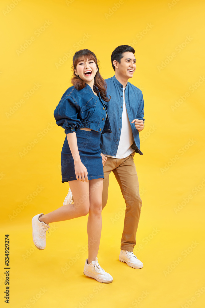 Portrait of funky couple jumping in air holding hands up enjoying time together isolated on yellow background