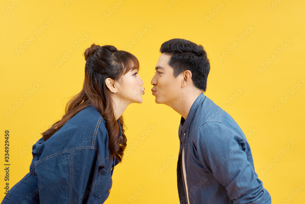 Profiles of girlfriend and boyfriend giving each other an air kiss over yellow Profiles of girlfriend and boyfriend giving each other an air kiss over yellow
