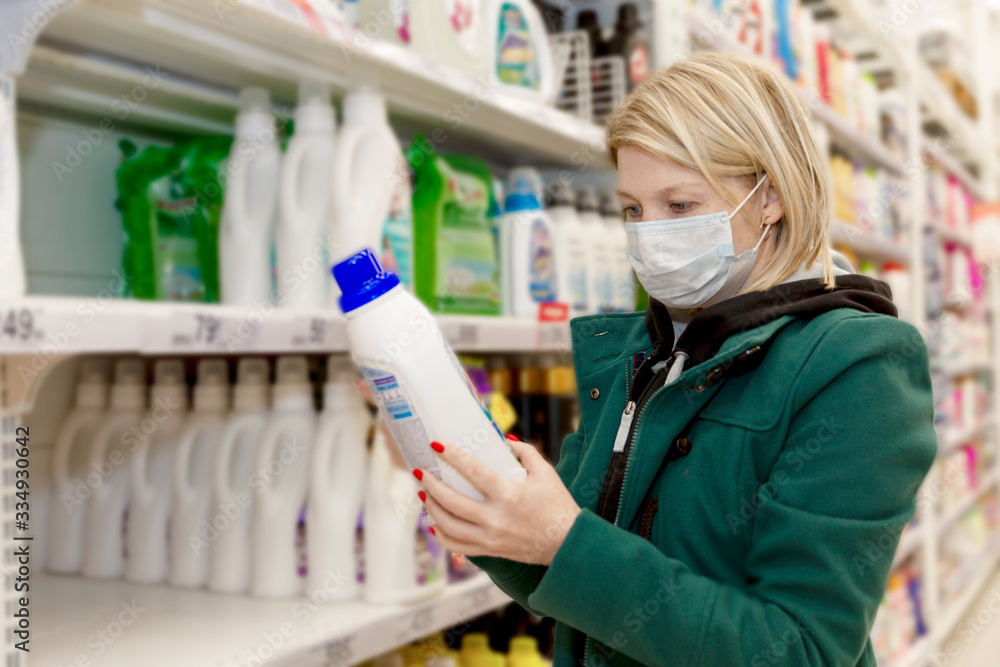 Blonde woman in medical mask chooses household chemicals in a supermarket. Quarantine during the coronavirus pandemic. Close-up.