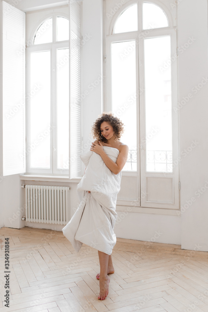 Beautiful sweet cheerful tender happy natural sleepy girl with Afro curls wrapped in a blanket wakes up and enjoys the morning looks out the window against the background of large vintage Windows Beautiful sweet cheerful tender happy natural sleepy girl with Afro curls wrapped in a blanket wakes up and enjoys the morning looks out the window against the background of large vintage Windows