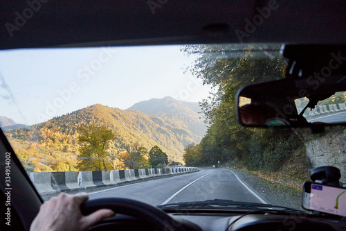 View from inside car window to the road and autumn mountain landscape. Asphalt road in perspective in a sunny day