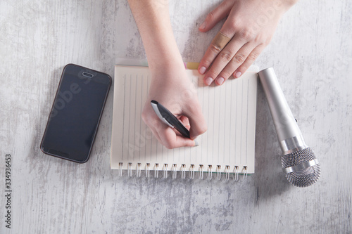 Girl writing on notepad. Microphone and smartphone on the desk