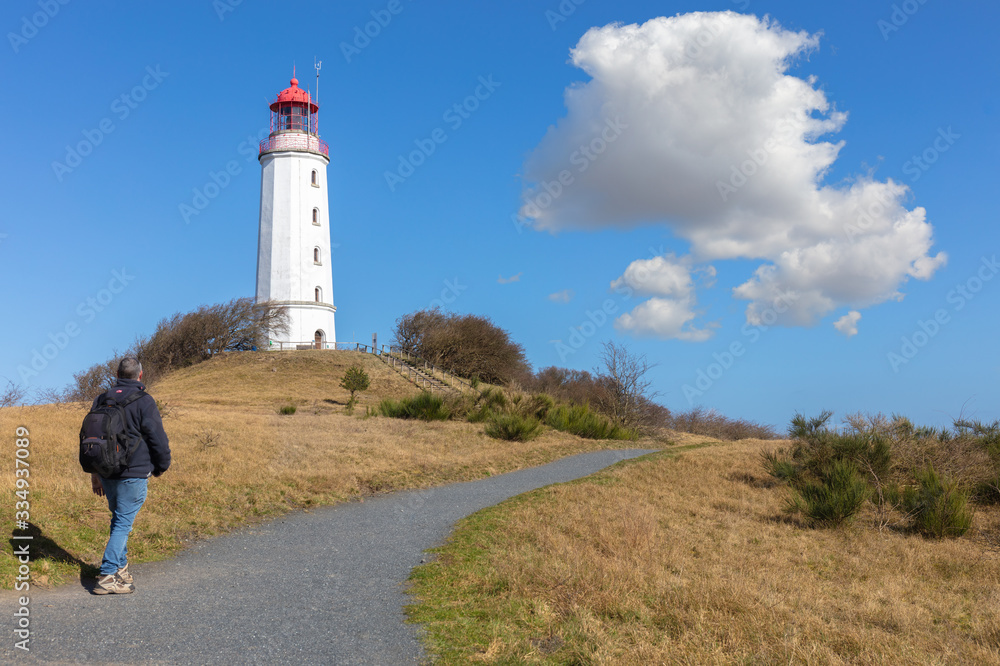 The Dornbusch lighthouse on the German island of Hiddensee in the Baltic Sea. It is a beautiful winter day with blue sky and clouds. In the foreground a hiker with a backpack.