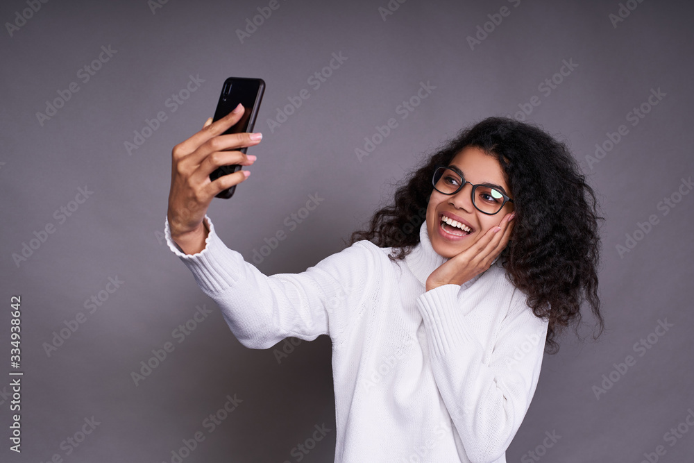 Beautiful dark-skinned girl takes a selfie on a gray background.