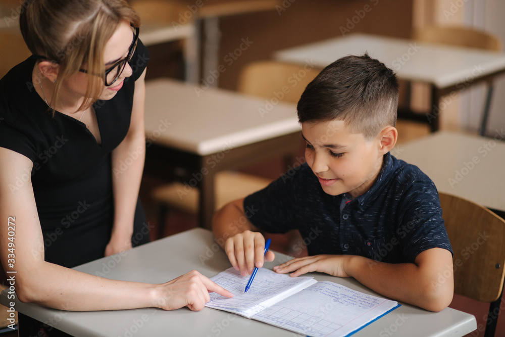 Teacher helping school kids writing test in classroom. education, elementary school, learning and people concept Teacher helping school kids writing test in classroom. education, elementary school, learning and people concept