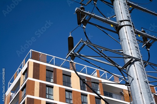 High voltage towers with electrical wires on apartment building background. 