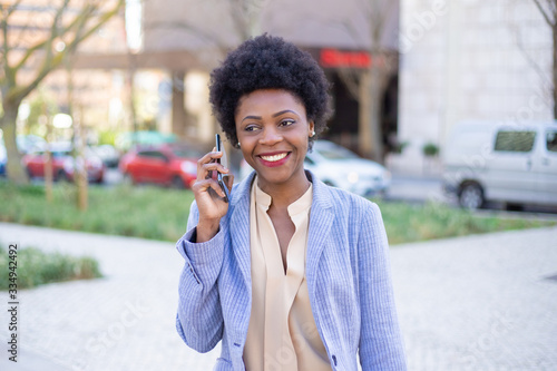 Beautiful smiling businesswoman talking on phone on street. Front view of confident African American woman communicating via smartphone. Technology, communication concept
