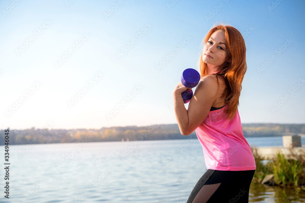 Pretty slim woman working with dumbbells near the lake. health and beauty concept. Pretty slim woman working with dumbbells near the lake. health and beauty concept.