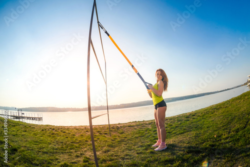 sport woman doing training outdoors with TRX at daytime. Total body resistance exercises for her healhty lifestyle