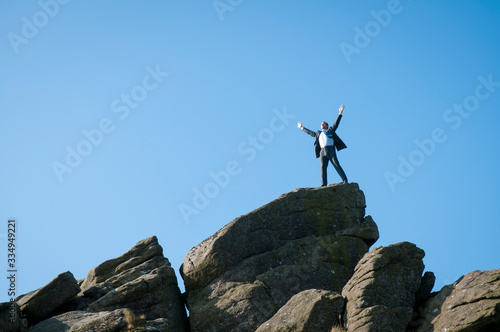 Distant businessman standing with his arms spread on a dramatic rocky mountaintop