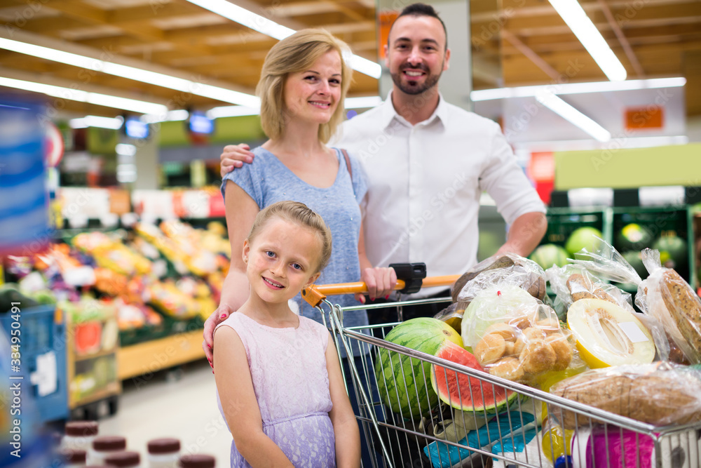 Glad parents with girl shopping in hypermarket