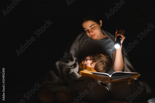 Happy family. Time for stories. Delighted happy cute mother and son enjoying a book before sleeping and using a flashlight.