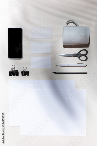 Sheets, gadgets and work tools on a white table indoors. Creative, cozy workplace at home office, inspirational mock up with plant shadows on surface. Concept of remote office, freelance, atmosphere.
