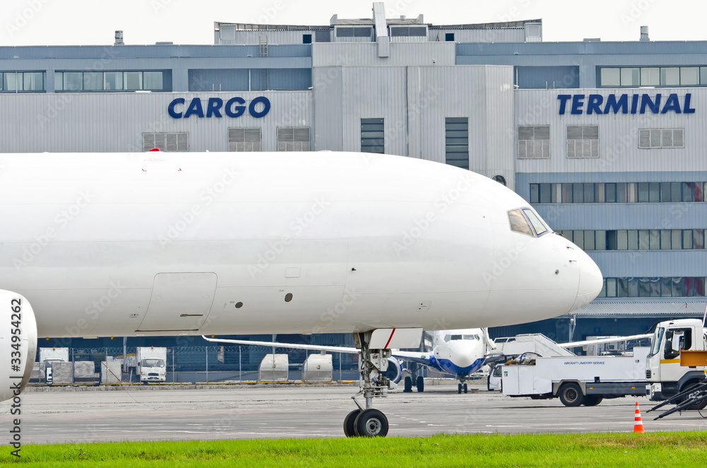 Freight cargo airplane in the parking lot of the airport, against the background of the cargo terminal of the aerodrome building.