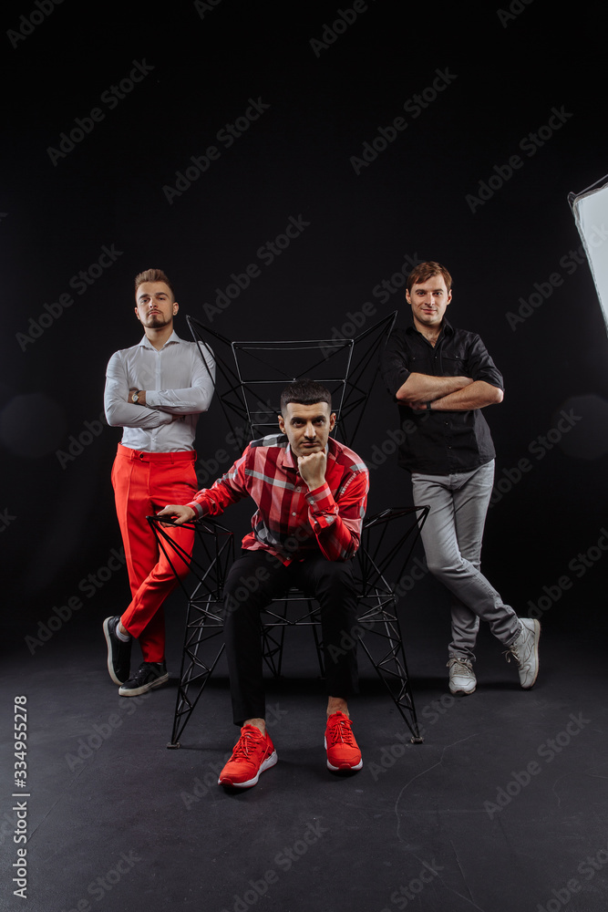 Fototapeta premium A team of three people poses in a photo studio. bright costumes. on a dark background. one is sitting on a chair.