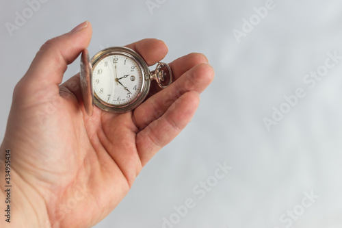 Mano sujetando reloj de bolsillo antiguo de plata sobre fondo blanco.
