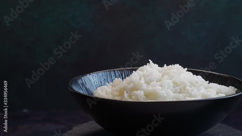 Freshly cooked rice in bowl with steam rotation on dark with copy space