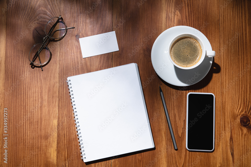 Gadgets, coffee, work tools on a wooden table indoors. Creative, cozy workplace at home office, inspirational mock up with plant shadows on surface. Concept of remote office, freelance, atmosphere.