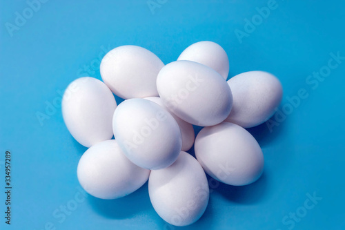 In the horizontal photo on a blue background in the center there are ten white chicken eggs. Eggs whole and raw