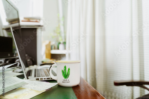 Home office workplace with open laptop, papers and a tea mug on wooden desk