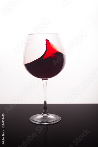 Red wine in a glass splashes on the walls of the glass on a white background.