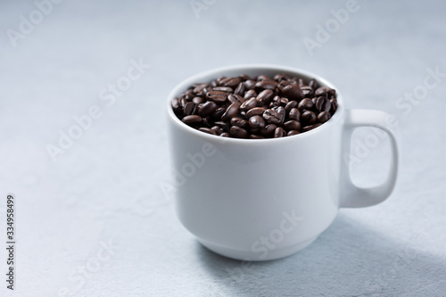 A view of a white mug full of coffee beans against a white marble background.