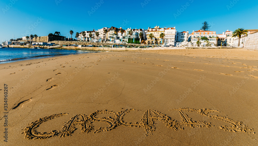 Empty idyllic sandy Praia do Ribeiro in Cascais, Portugal with the words Cascais written on sand