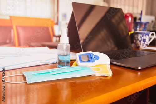 Work from home concept alcohol spray bottle and thermometer on table with surgical mask virus protection.