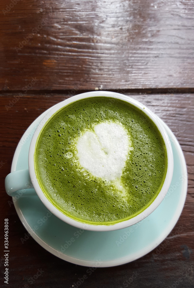 Matcha green tea latte with heart shape of decoration milk in white mug on wooden desk table at loft style coffee shop, commercial advertisement backgrounds Matcha green tea latte with heart shape of decoration milk in white mug on wooden desk table at loft style coffee shop, commercial advertisement backgrounds