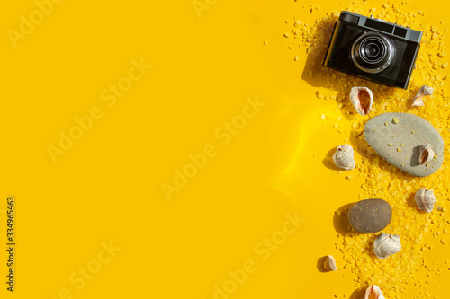 Flat lay travel or vacation. Camera, shells and stones on a bright yellow background. Summer background with accessories for travelers and bright sunlight.