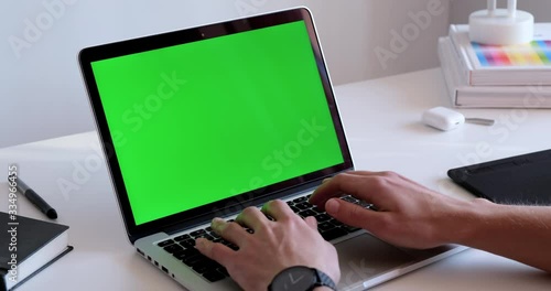 Man hands typing on a laptop keyboard with green screen chroma key mockup in a workplace office environment. Male working, using an application, surfing the web, programming, coding on a computer