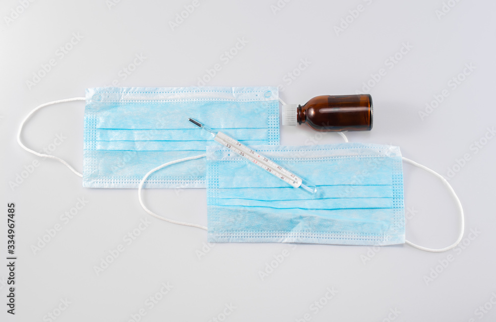 Medical banner of face masks, a thermometer for measuring body temperature and a glass bottle on a gray background, top view Medical banner of face masks, a thermometer for measuring body temperature and a glass bottle on a gray background, top view