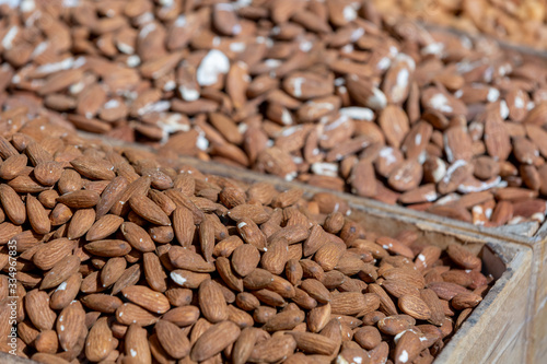 Clump of almond in tray on sunlight at food market, selective focus on foreground, blurred nuts on background