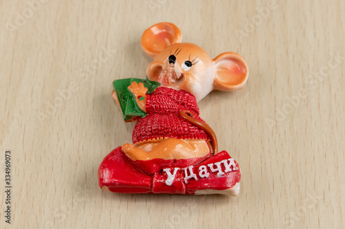 
A souvenir is a mouse of luck from porcelain in the year of a metal rat on a light wooden background