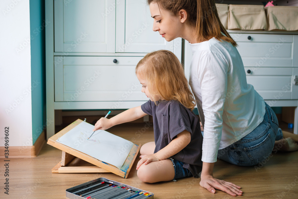 Mom and daughter draw with pencils and paints while sitting on the floor in the games room. Mom and daughter draw with pencils and paints while sitting on the floor in the games room.