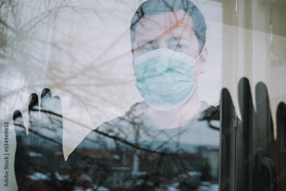 man looking trough window with mask and gloves in isolation protecting from coronavirus covid-19