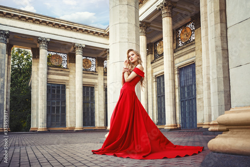 Billede på lærred Beautiful blonde girl in a red long dress on a background of architecture, colum