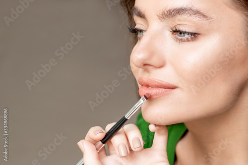 Makeup artist applies lipstick on face of beautiful woman  makeup in process.