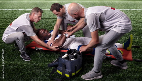 Sport doctors provide first aid to an injured player on a professional soccer stadium.