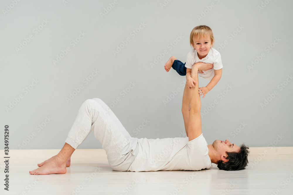 Naklejka premium Happy loving father lying on a floor of an apartment, lifting his baby in the air. Smiling, laughing.